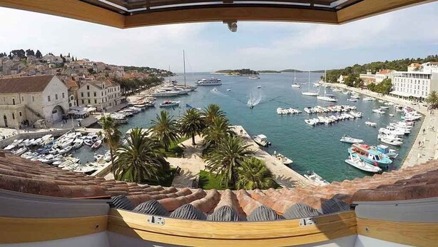 A panoramic view of a marina with numerous boats docked, palm trees, and buildings along the waterfront. - Hvar Attic Apartment (Hvar)