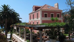 A red building with a tiled roof, surrounded by palm trees and potted plants. - Hvar Attic Apartment (Hvar)