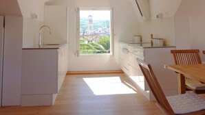 A compact kitchen with a view of a tower through a window, wooden flooring, and a dining area with a table and chairs. - Hvar Attic Apartment (Hvar)