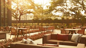 An outdoor seating area with tables and chairs, surrounded by trees and plants.