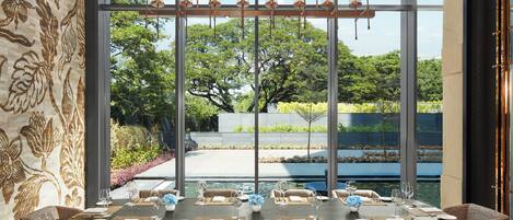 A dining area with a view of a garden and pool, featuring a long table set for six with chairs.