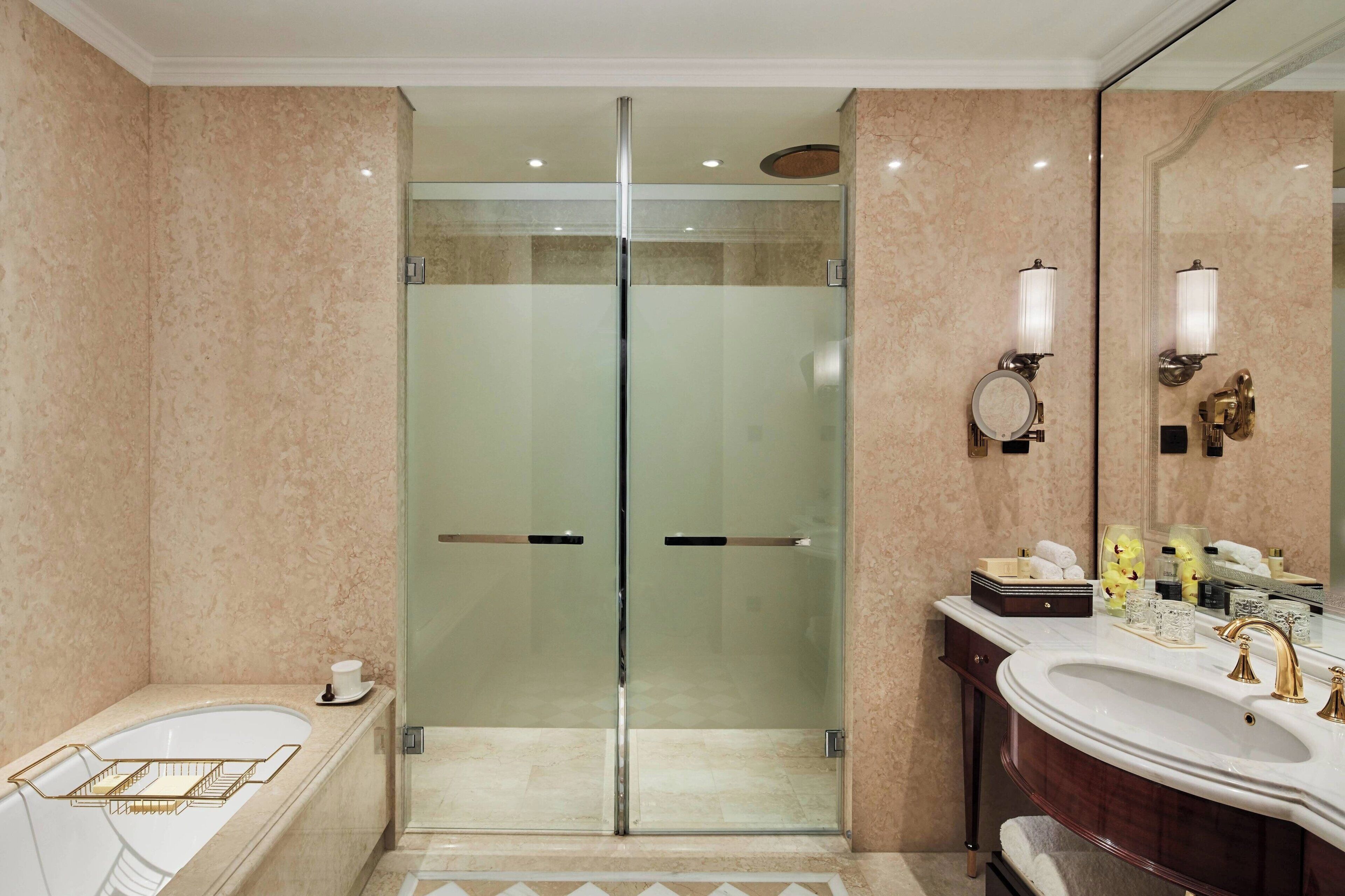 Een moderne badkamer met een douchecabine van glas, een vrijstaand bad en een wastafel met een grote spiegel en verlichtingsarmaturen.