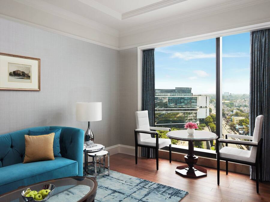 Un salon moderne avec un canapé bleu, une table ronde et deux chaises. Un tableau encadré est accroché au mur, et une fenêtre offre une vue sur la ville.