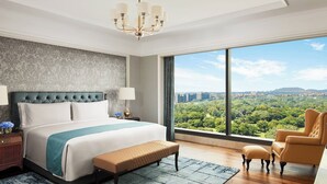 A modern hotel room with a large bed, a view of a cityscape, a chandelier, and a city park view. - The Ritz-Carlton, Pune (Pune)