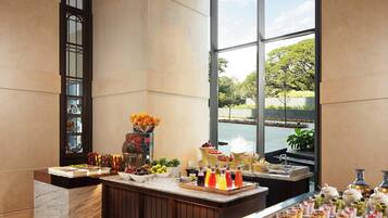 A buffet area with a variety of food and drink options, a marble counter, and a view of a body of water through large windows.