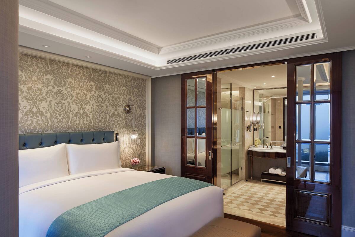 A hotel room with a large bed, a bathroom with a glass shower, and a view through an open door.