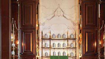 Un lobby lujoso con pared de mármol, paneles de madera y una pantalla verde. Hay zonas de estar con mesas y sillas, y un área de bar con estantes llenos de botellas.