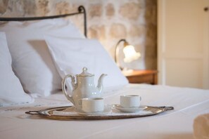 A neatly made bed with white linens, a white teapot, two white cups, and a tray on a textured doily.