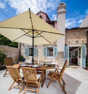 An outdoor dining area with a table and chairs, a large umbrella, and a stone building in the background.