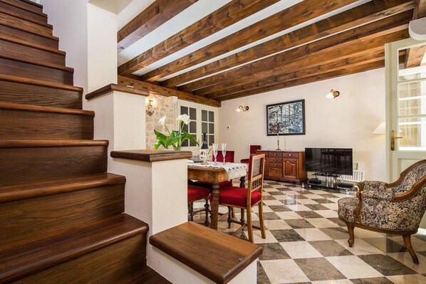 A staircase with wooden steps leading to a dining area with a checkered floor, a table set for two, and a television in the background.