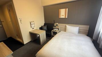 A hotel room with a bed, bedside table, nightstand, and a small seating area with a chair and a sofa.