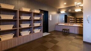 A hotel room with a checkered floor, wooden shelving with baskets, a small stool, and a bathroom with a sink and mirror. - Hotel Route-Inn Kanuma Inter (Kanuma)