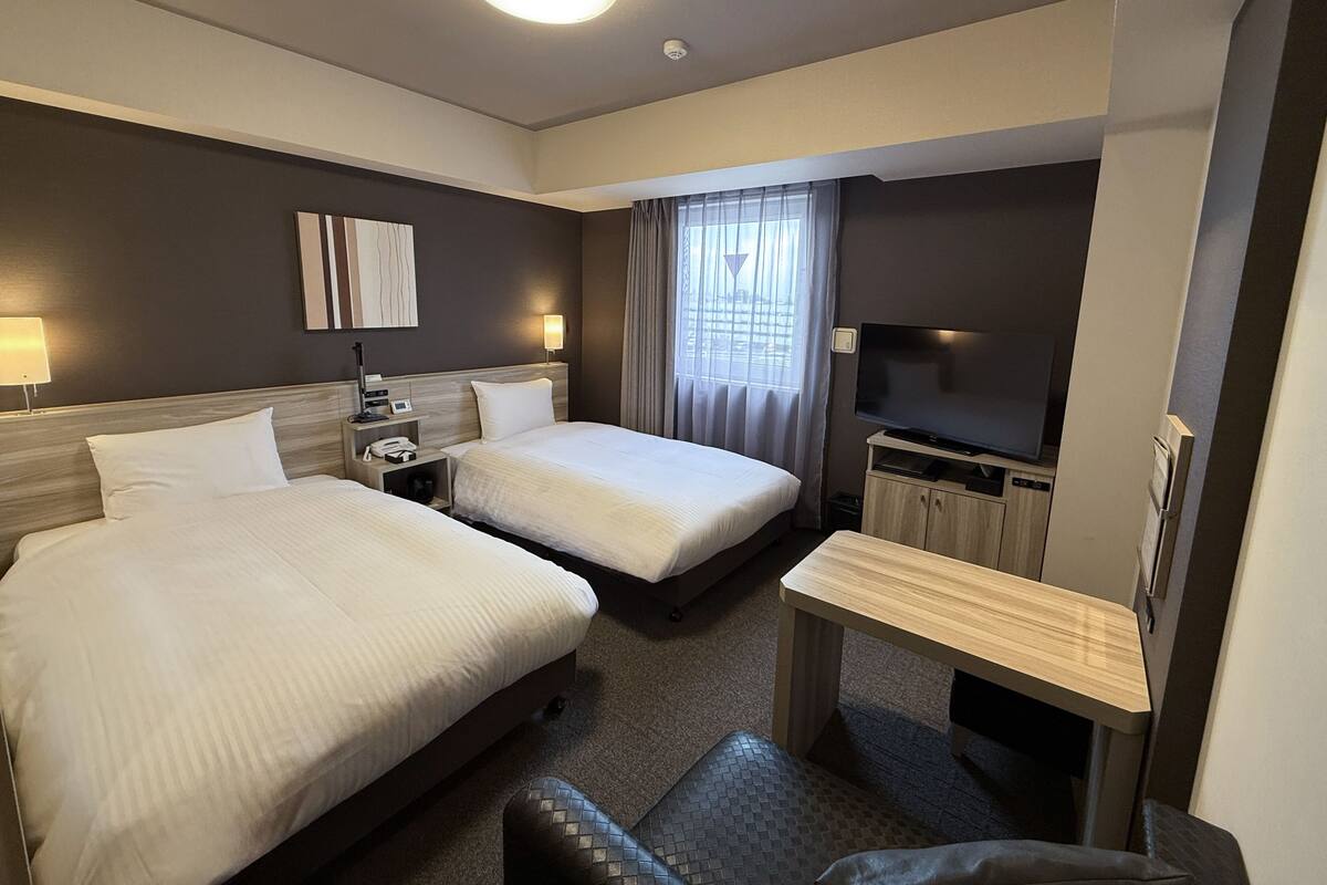 Une chambre d’hôtel avec deux lits, un bureau, une télévision et une fenêtre avec des rideaux.