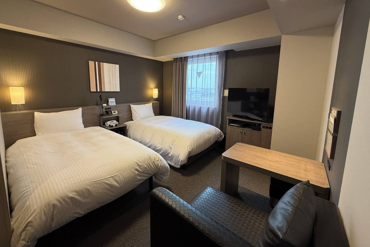 Une chambre d’hôtel avec deux lits, un bureau, une télévision et une fenêtre avec des rideaux.