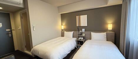 Ein Hotelzimmer mit zwei Betten, einem Nachttisch mit Lampe, einem Wandtelefon und einer Deckenleuchte.