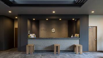 Un espace d’accueil avec un mur recouvert de carreaux, deux tabourets en bois et un comptoir de réception.