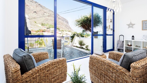A room with wicker furniture, a glass door leading to a balcony, and a view of a mountainous landscape. - Casa Sirena (Santa Cruz de Tenerife)