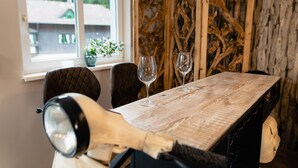 Una mesa de comedor con dos copas de vino, una planta en maceta y un panel decorativo de madera en una habitación con ventana.
