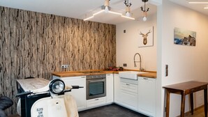 Una cocina moderna con armarios blancos, una encimera de madera y un horno empotrado. En un lateral, paneles de madera y un cuadro con ciervos en la pared.