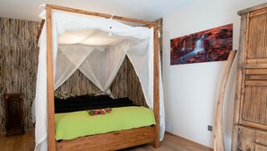 Una cama con dosel de madera, con un edredón verde y dosel blanco, un armario de madera y un cuadro colgado en la pared.