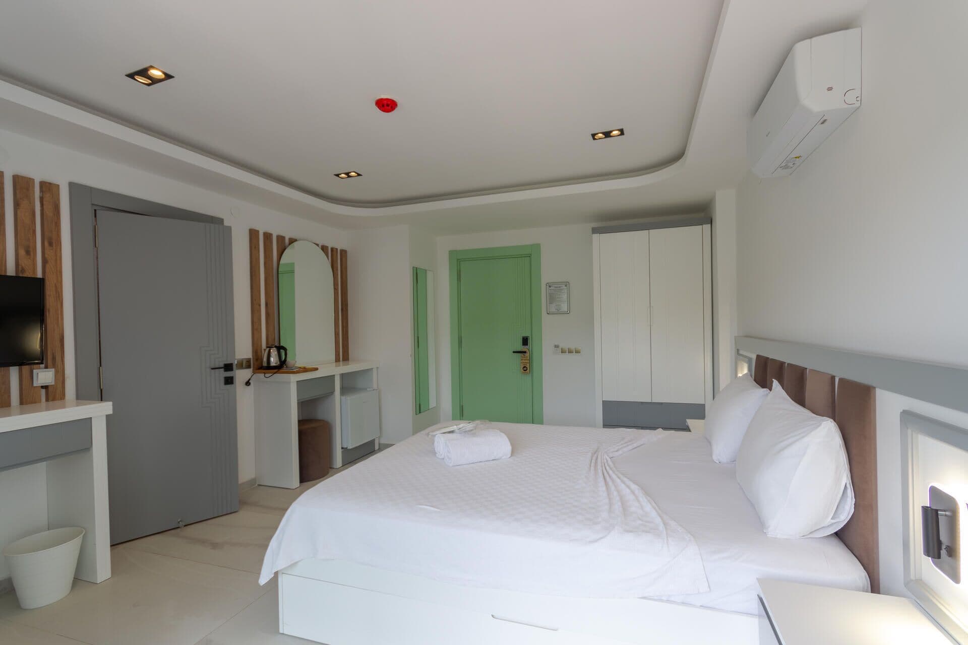 A hotel room with a bed, a desk, a television, and a green door.