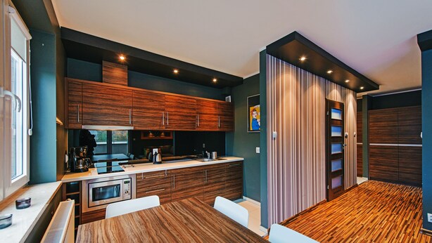 A modern kitchen with wooden cabinets, a built-in microwave, and a dining area with a wooden table and white chairs. - Apartamenty Sun & Snow Bursztynowy (Wladyslawowo)