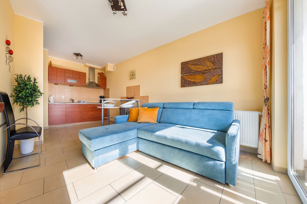 Ein Wohnzimmer mit einem blauen Ecksofa, einem Esstisch und einer Küche im Hintergrund.