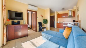A modern living room with a blue sofa, a flat-screen TV, and a wooden cabinet. - Apartamenty Sun & Snow Bursztynowy (Wladyslawowo)