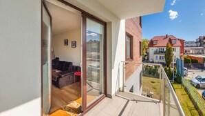 A balcony with a sliding glass door leading to a living area with a sofa and a red chair. - Apartamenty Sun & Snow Bursztynowy (Wladyslawowo)