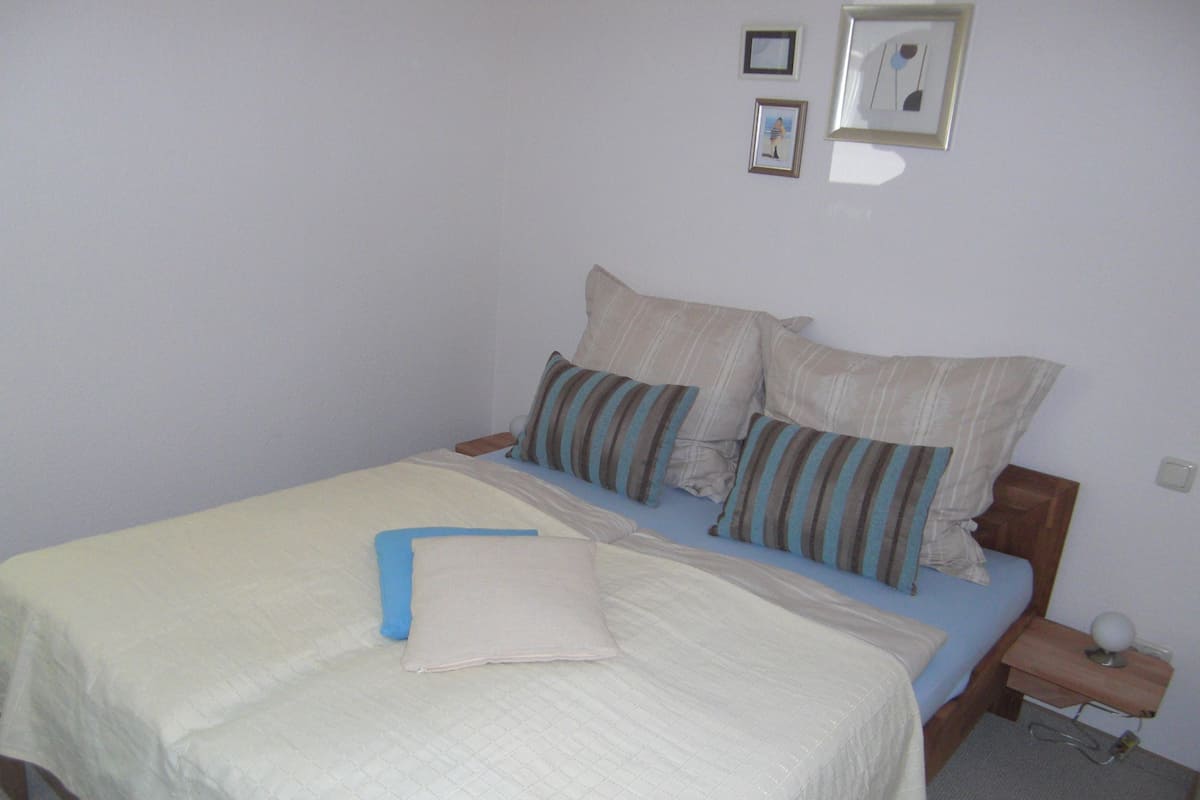 Un dormitorio con cama, almohadas, una mesita de noche con lámpara y cuadros enmarcados en la pared.