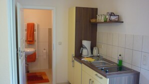 A compact kitchen with a sink, a coffee maker, and a shelf with kitchen items.