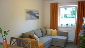 A living room with a grey sofa, a wooden table, and a window with curtains.