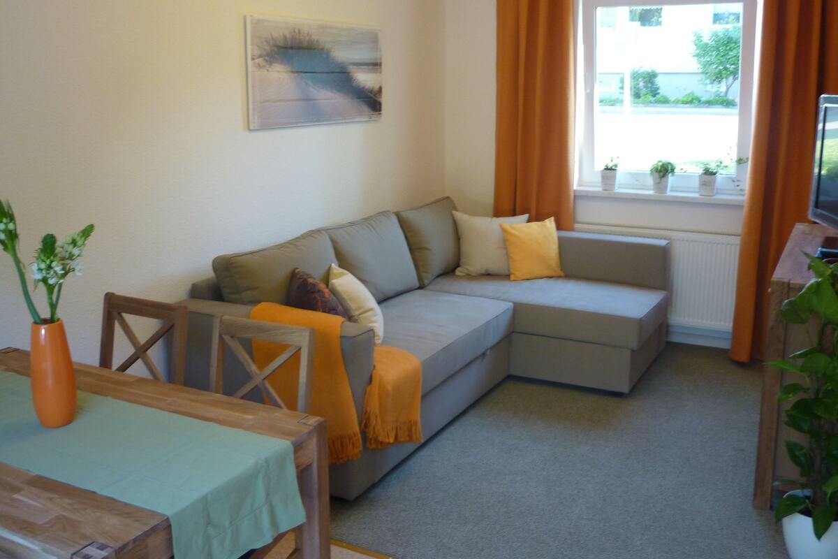 Una sala de estar con un sofá gris, una mesa de madera y una ventana con cortinas.