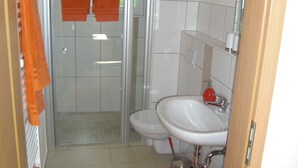 A bathroom with a shower, toilet, and sink. There are orange towels hanging on the wall.