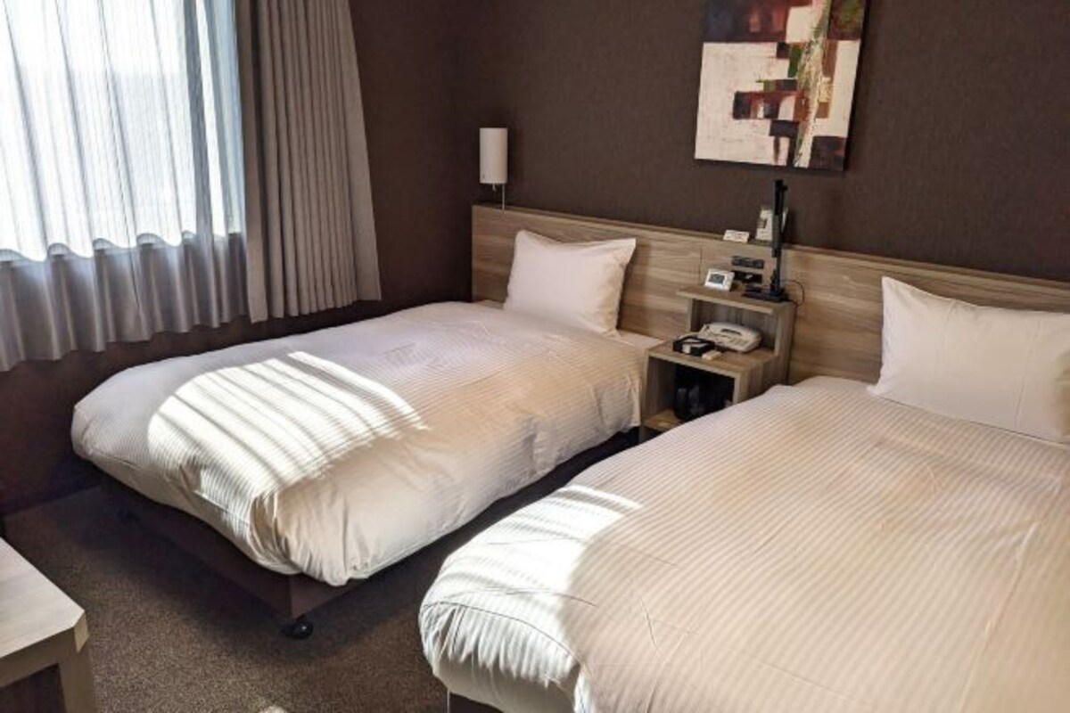 Habitación de hotel con dos camas, una mesita de noche con lámpara y una obra de arte en la pared.