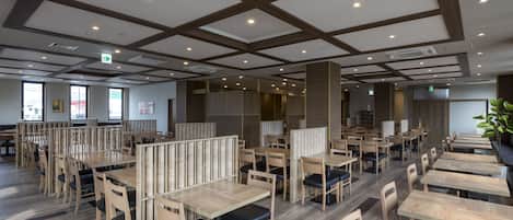 A modern restaurant with wooden tables and chairs, high ceilings with exposed beams, and large windows allowing natural light.