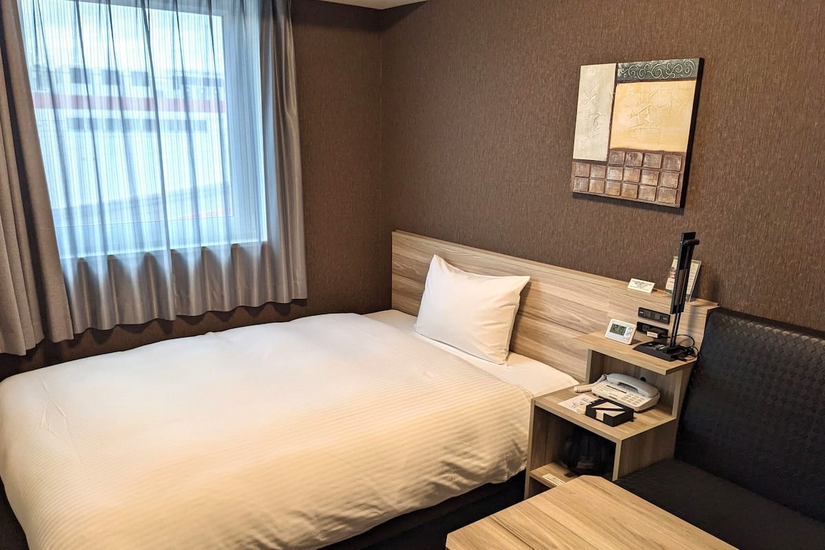 A hotel room with a large bed, a bedside table with a phone, a small table, and a couch.