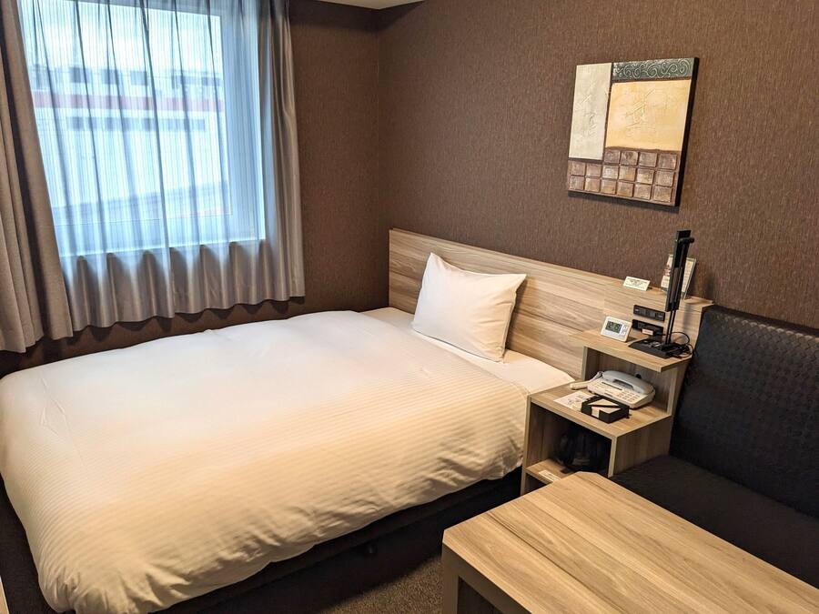 Ein Hotelzimmer mit einem großen Bett, einem Nachttisch mit Telefon, einem kleinen Tisch und einem Sofa.