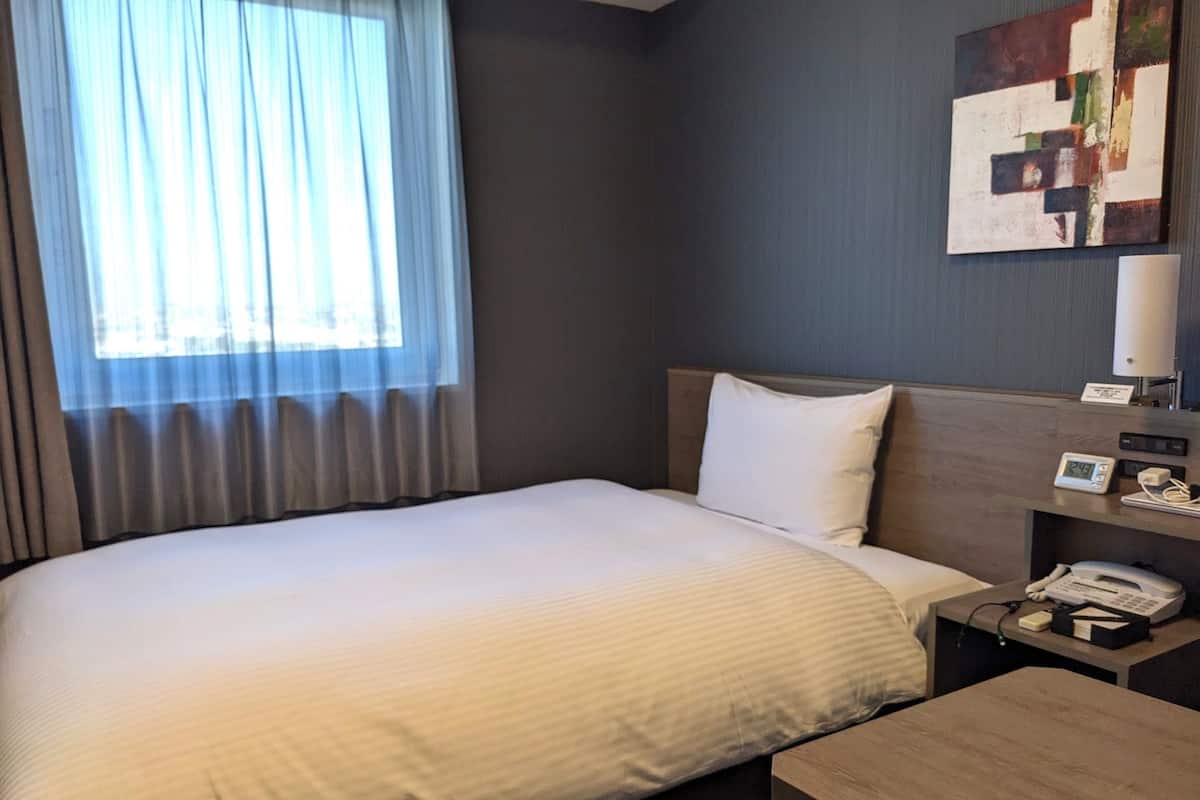 A hotel room with a large bed, a bedside table with a phone, and a painting on the wall.