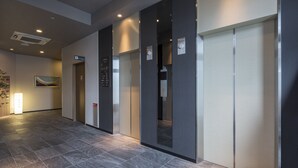 Área de elevador moderna, com piso ladrilhado, ar condicionado na parede e uma porta com sinal acima.