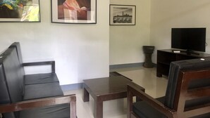 Uma sala de estar com sofá, mesa de centro, TV e quadros nas paredes.