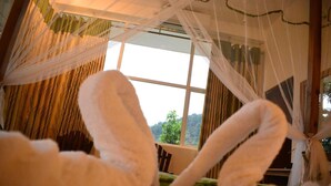 Ein Zimmer mit großem Fenster, einem Bett mit weißer Bettwäsche und Blick auf Grün.