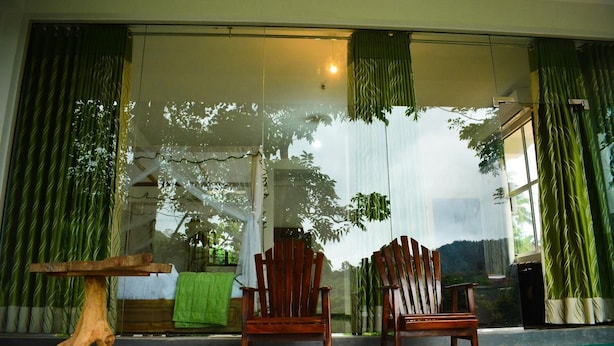 Ein Zimmer mit zwei Holzstühlen, einem Holztisch und einem großen Fenster mit Vorhängen.