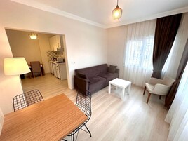 Un apartamento moderno con comedor, sofá, una mesita y una cocina al fondo.