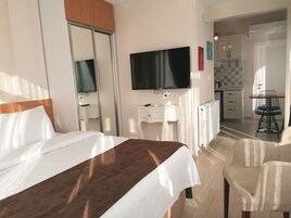 Habitación de hotel con cama, escritorio, televisor y vista a la cocina.