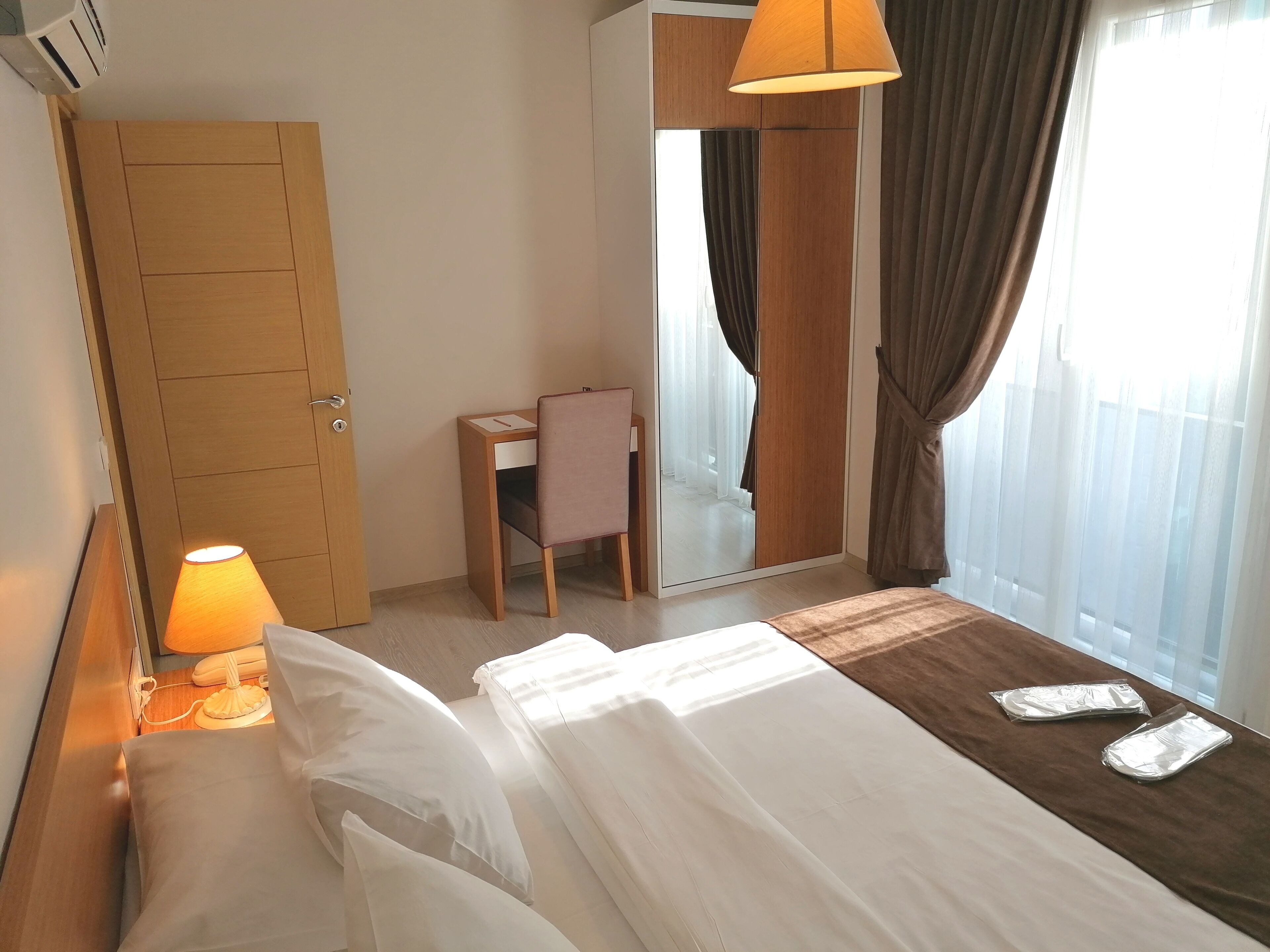 A hotel room with a bed, bedside lamp, desk, chair, and a large mirror.