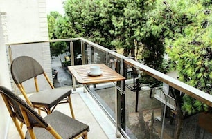 A balcony with wicker chairs and a table, overlooking a garden with dense foliage.