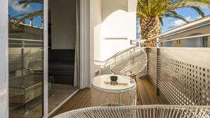 Un balcon avec une table en verre, des meubles en osier blancs, un palmier et une vue sur le ciel.
