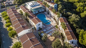 Vue aérienne d’un complexe hôtelier comprenant une piscine centrale, plusieurs villas et une zone de plage.