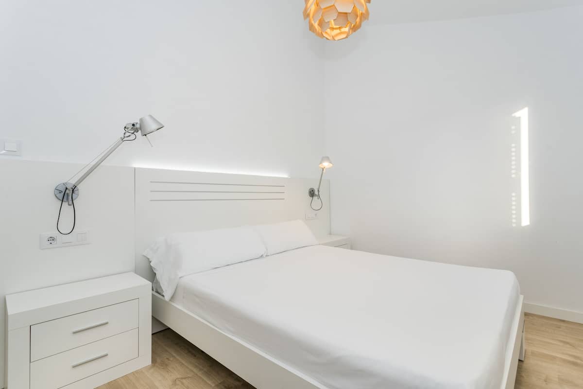 Un dormitori minimalista amb un llit individual, taules de nit i làmpades penjades a la paret.